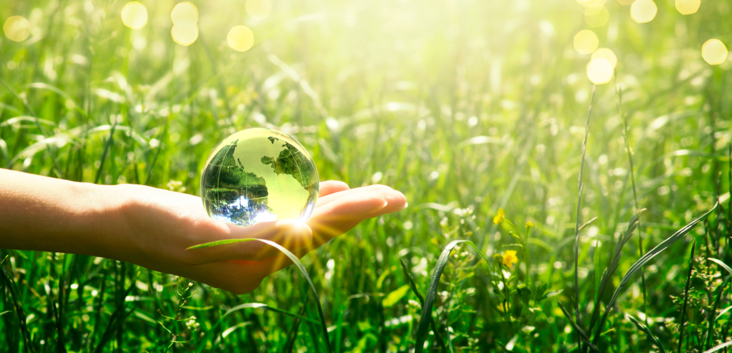 Earth crystal glass globe in human hand on fresh juicy grass background. saving environment and clean green planet concept. card for world earth day.
